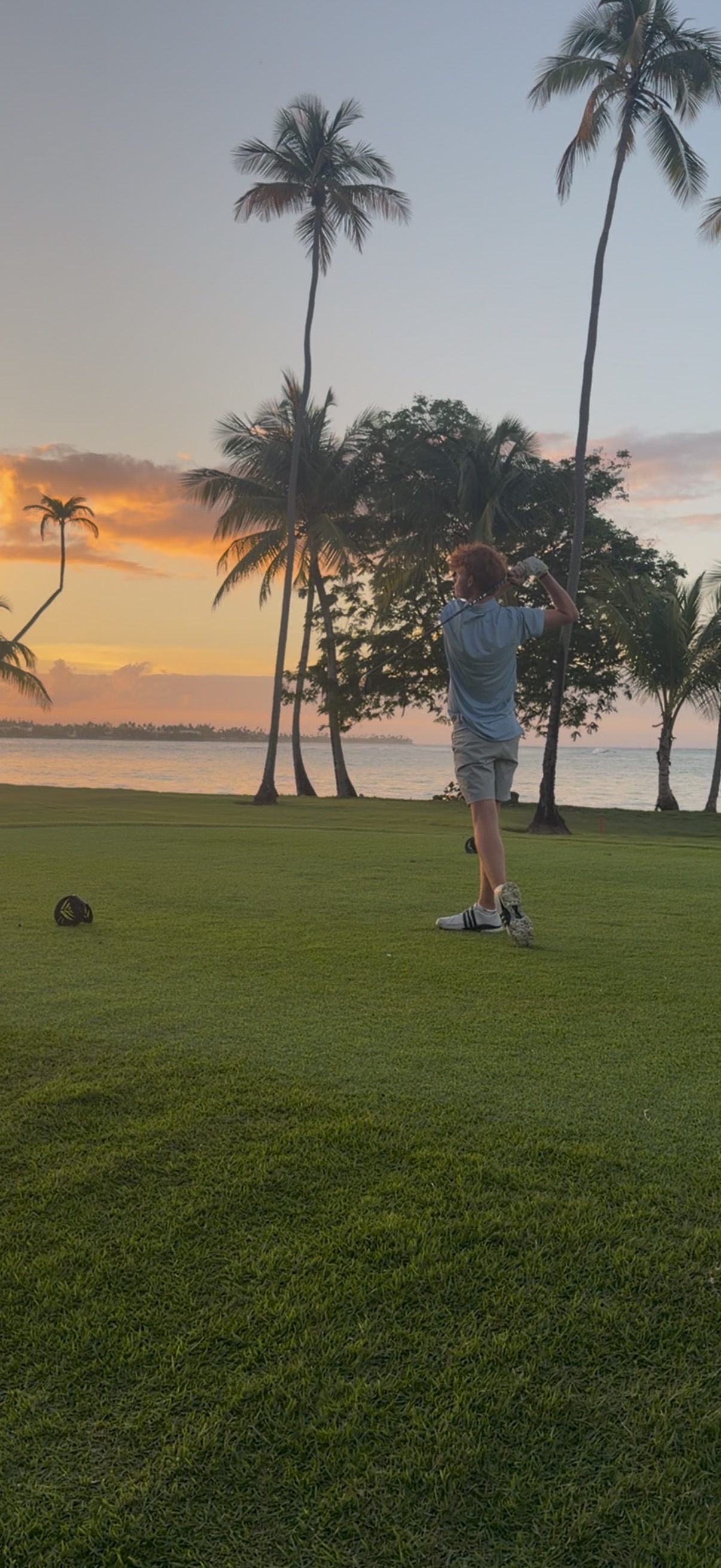 Willy finishing a golf swing on a coastal course at sunset